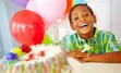 Photo of young boy at his birthday party, colourful balloons in the background