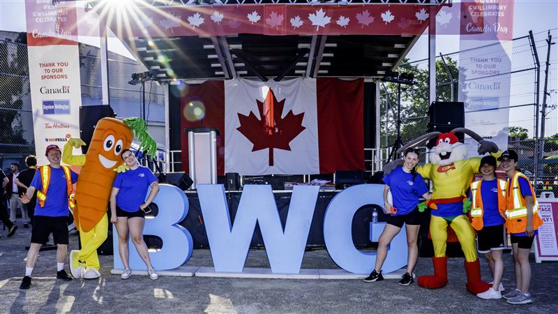 Image of Canada Day stage with BWG staff posing Gwilly mascot and Captain Carrot mascot