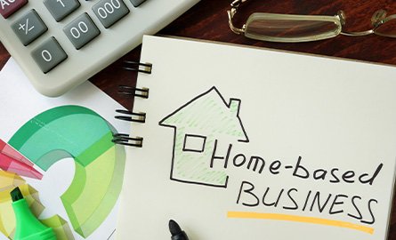 Partial vie of calculator, eye glasses, writing utensils, and a sketchbook with a drawing of a home and the words "Home-based Business"