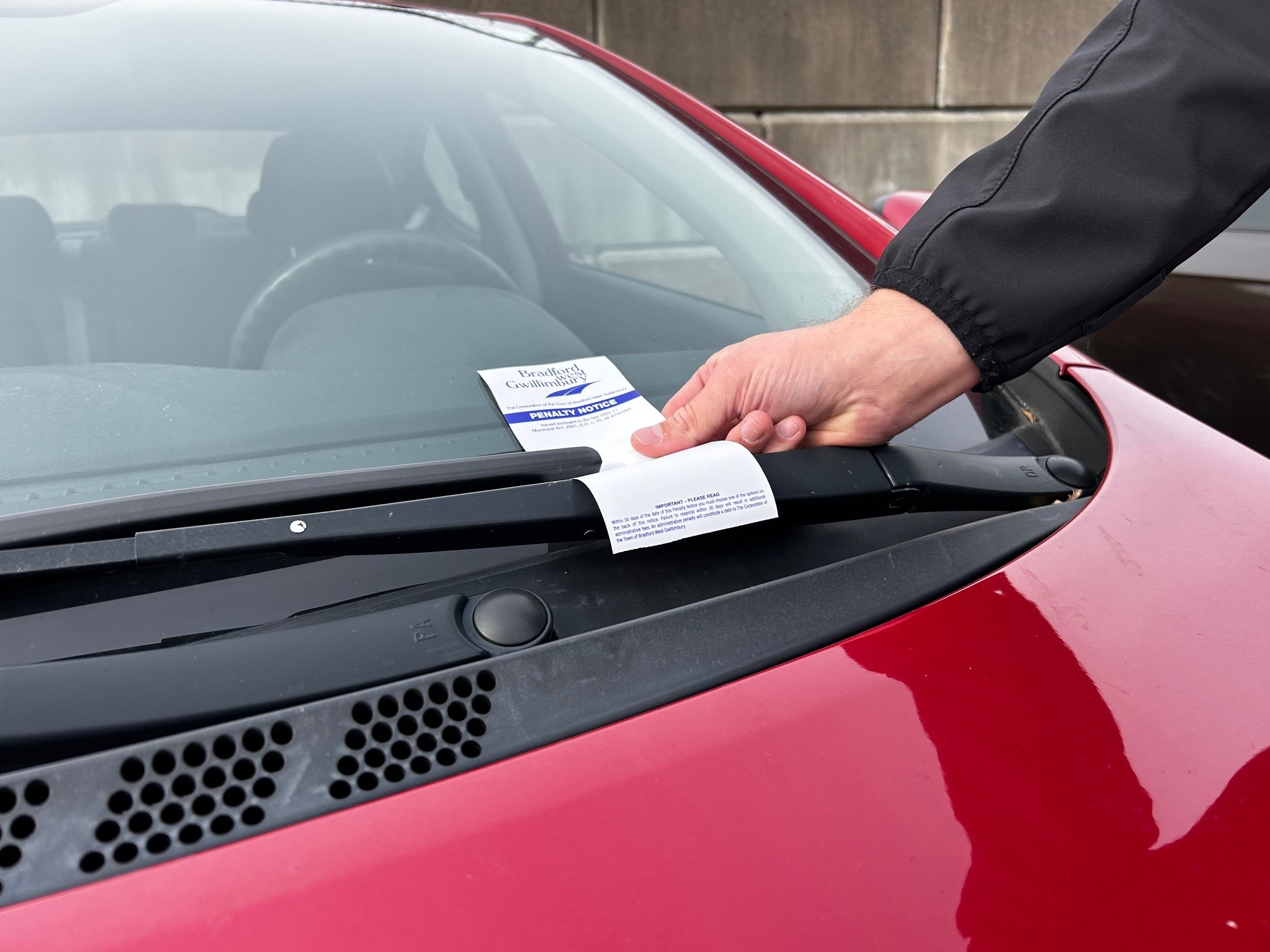 Enforcement officer putting a parking ticket on the front windshield of a red car.