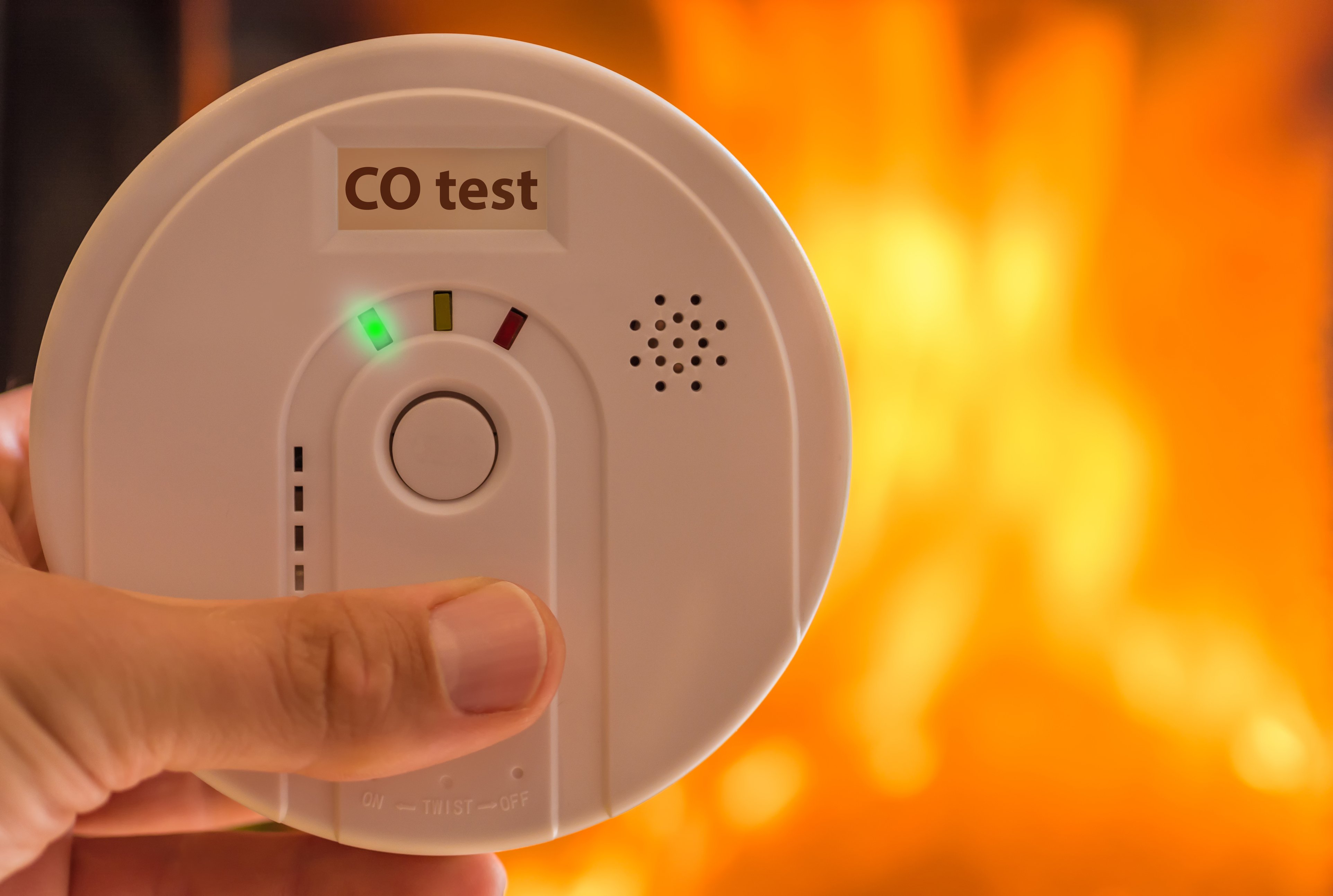 hand on test button of a carbon monoxide detector with flames in background
