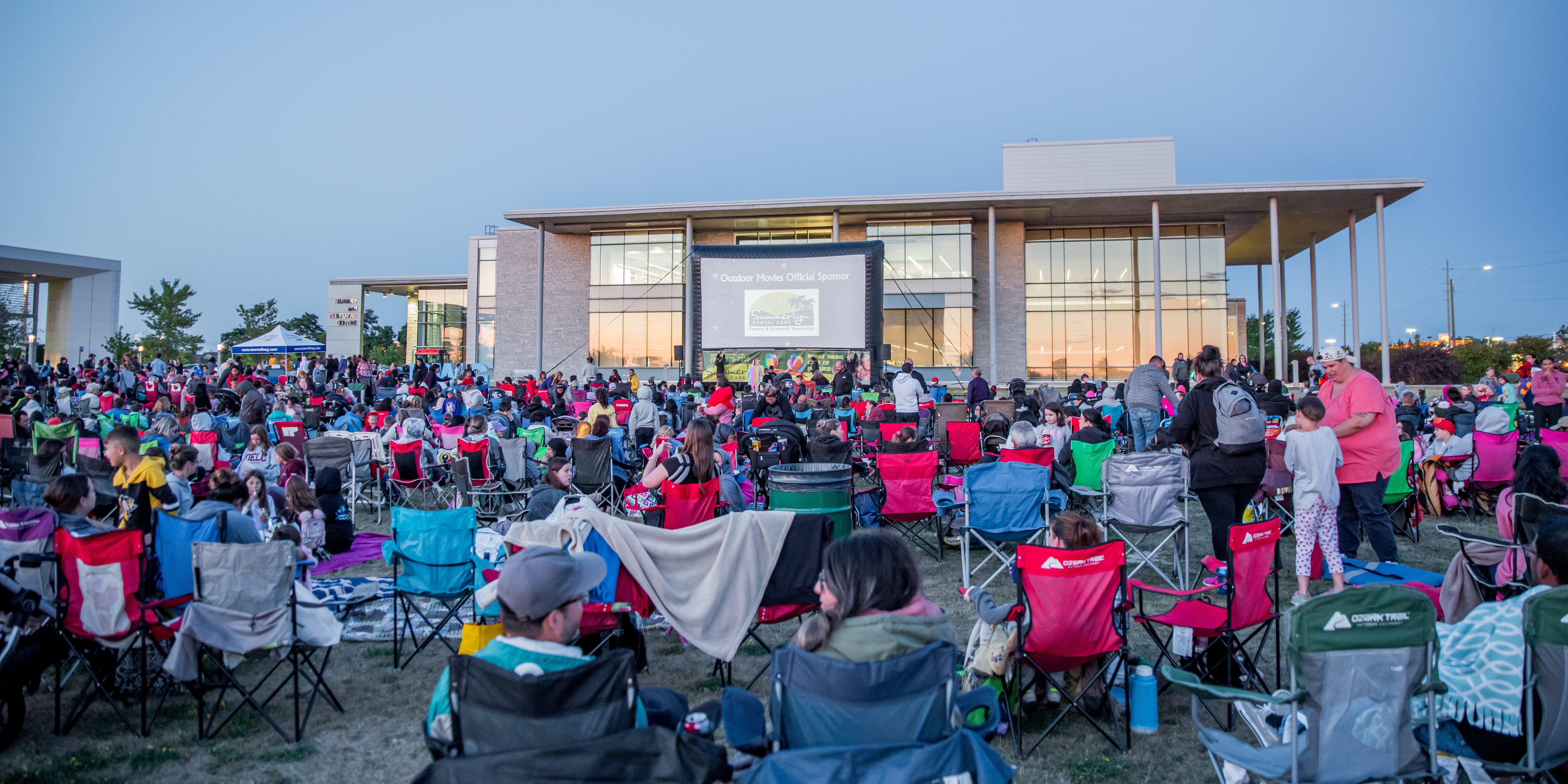 Residents gathered outside sitting in lawn chairs watching a movie at the Town of BWG Civic Centre Residents gathered outside sitting in lawn chairs watching a movie at the Town of BWG Civic Centre