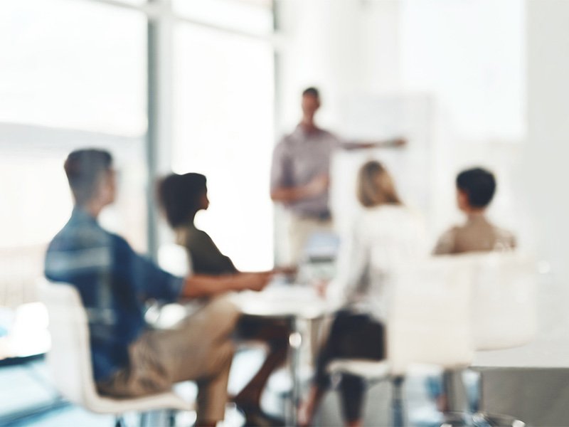 A group of people sitting around a desk while one person is presenting 