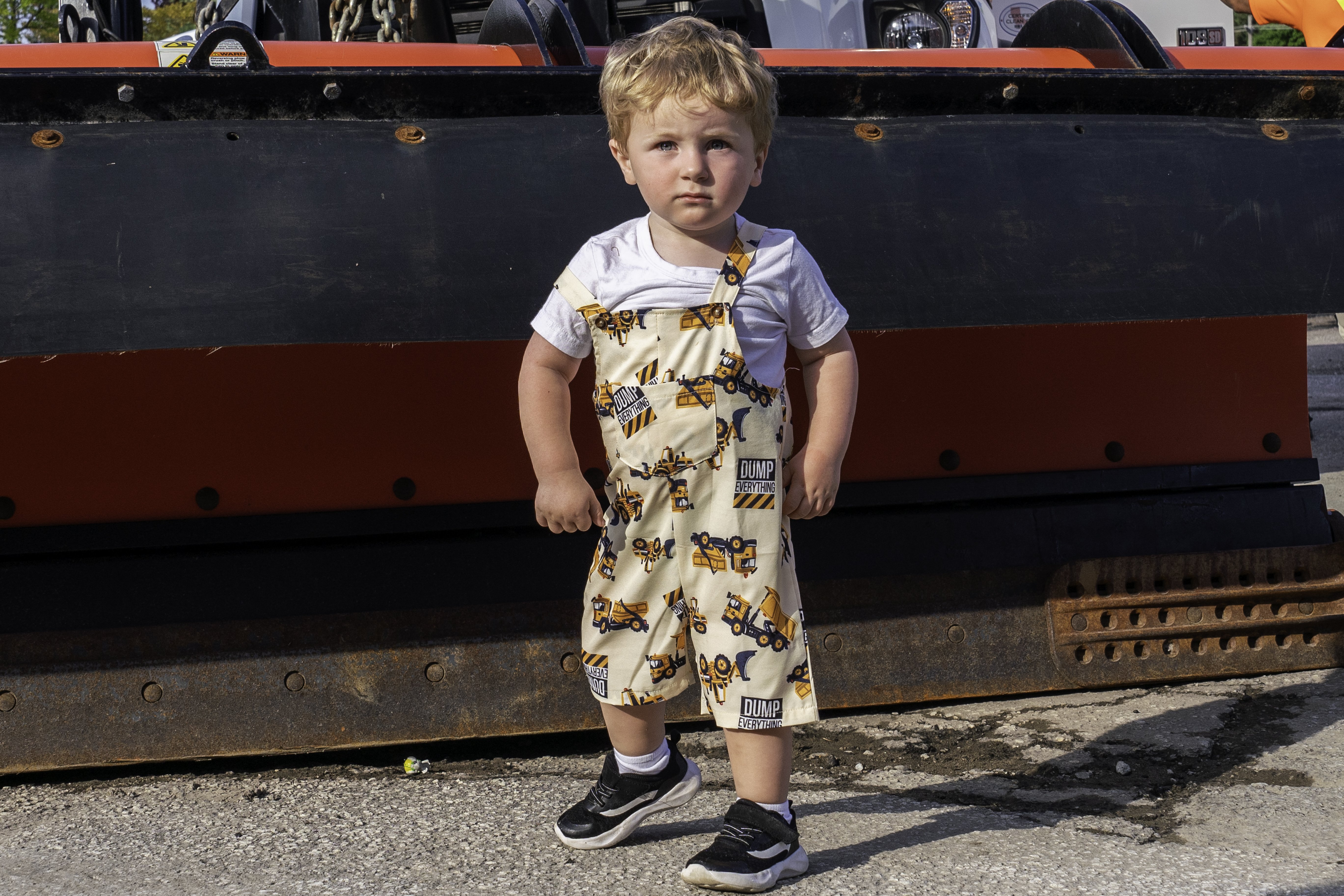 Little boy with truck overalls in front of the front of a red truck