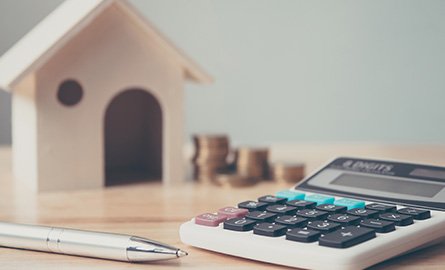 Desk surface with calculator, pen, coins, and a wooden house